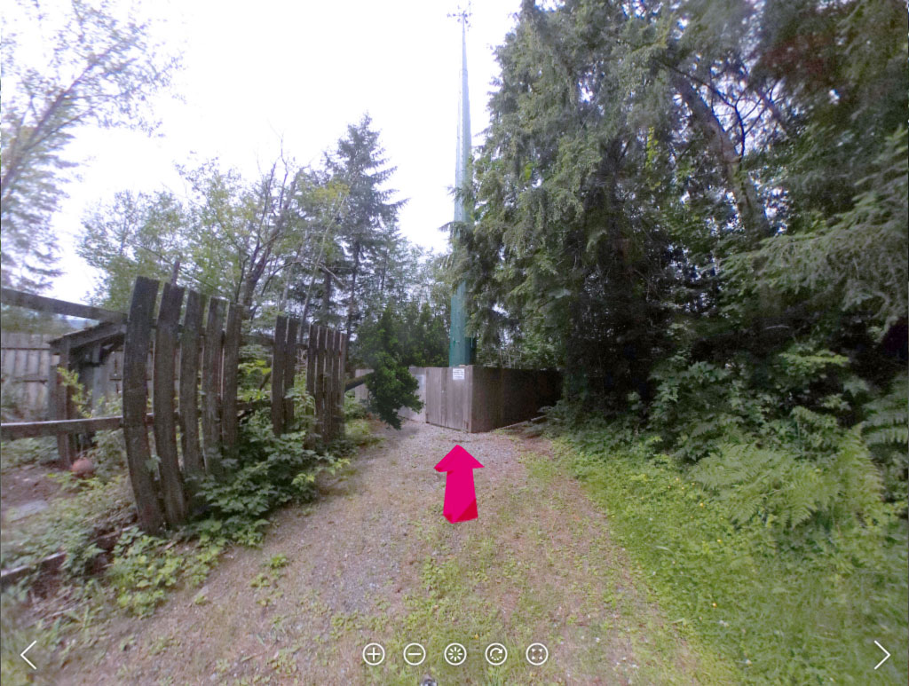 A 360-degree scene of a gravel path leading through trees to a fenced cell tower, with a magenta arrow pointing the way forward.